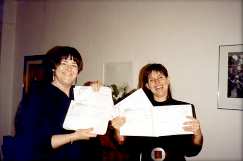 Beth Reynolds and former Associate Director Anne Bermonte smile while holding up pieces of paper
